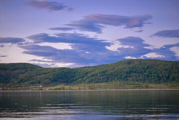 A large lake with calm waters at the edge of a picturesque tall forest in a village far from the cities