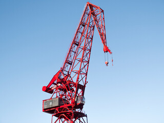 a red crane against a clear blue sky, its structure and machinery detailed, evoking a sense of industrial efficiency