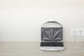White opened sandwich maker with black nonstick surface with plug in wall outlet socket on table...