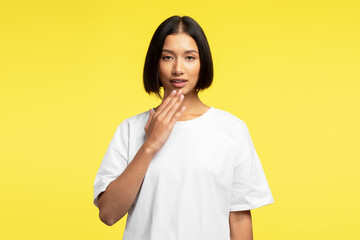 Attractive smiling Asian woman wearing white t shirt, gesturing standing on yellow background
