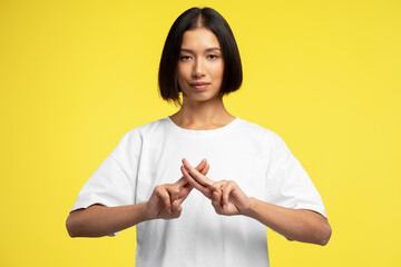 Portrait cheerful Asian woman wearing white t shirt, gesturing with fingers, ban, looking at camera