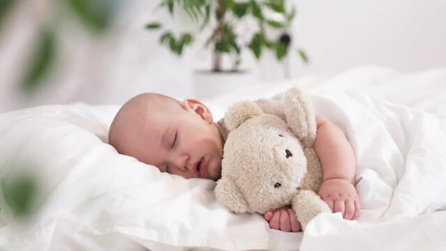 Gentle video of sleeping little boy hugging teddy bear on white bed cushion on white background sleeping baby