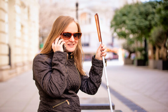 A visually impaired woman sitting on a bench in the city and using her smartphone