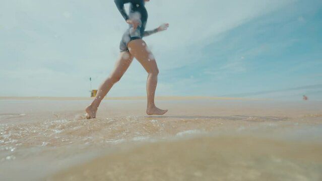 Girl running on the white sand beach, water splashing into the camera slow motion, rescue cabin in the background