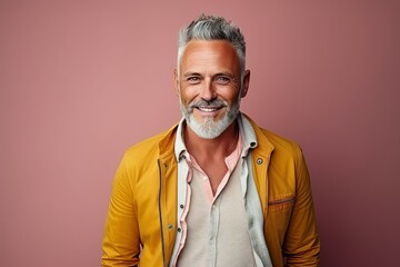 Portrait of a handsome senior man smiling at the camera while standing against a pink background. - Powered by Adobe