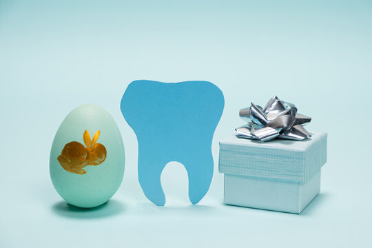Greeting card for dentistry happy Easter, tooth with painted egg and gift on a blue background