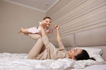 Happy Caucasian mother lifting in air cute little child girl and playing together in bedroom
