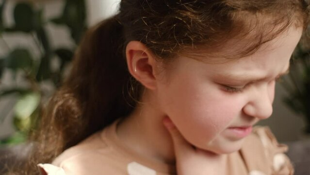 Close up portrait of unhealthy upset preteen girl kid sitting on couch at home holding neck, suffering from painful feelings in throat, angina, hard to swallow, voice loss. Child immunity concept