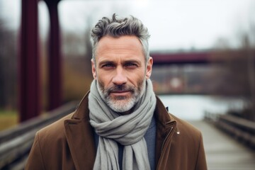 Portrait of a handsome mature man with gray beard wearing a brown coat and gray scarf. - obrazy, fototapety, plakaty