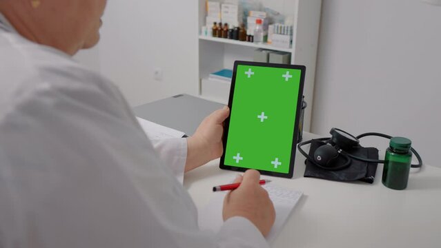 Doctor holds green screen mockup vertical tablet on the desk in office. Telemedicine concept female doctor use green screen tablet pc to see the patient and give advice.