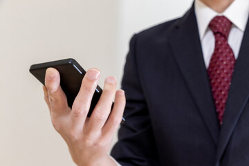 片手にスマートフォンを持つスーツ姿の男性	
