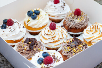 Assorted cupcakes in gift box with chocolate, vanilla and oreo cream, whipped meringue, raspberry, blueberry and bites of chocolate