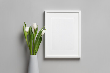 Blank vertical frame mockup with white fresh tulip flower in vase over grey wall background