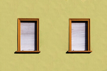 yellow plaster wall of an old house with window and closed shutter blinds