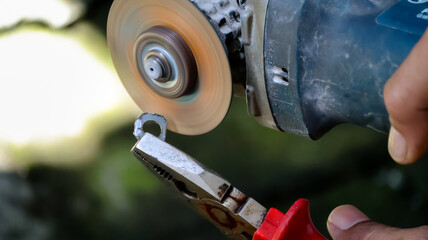Close-up of a worker is pinching a piece of metal with a pair of pliers and grinding it with an...