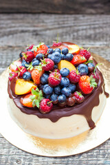 Delicious cheesecake with melted chocolate, apples, strawberries, blueberries, peaches, raspberries and kumquats on the top, rustic background