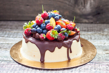 Delicious cheesecake with melted chocolate, apples, strawberries, blueberries, peaches, raspberries and kumquats on the top, rustic background
