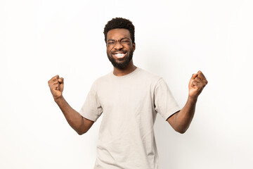 Portrait of a happy African American man celebrating with fists raised, exuding joy and victory over a light background. - 745840655