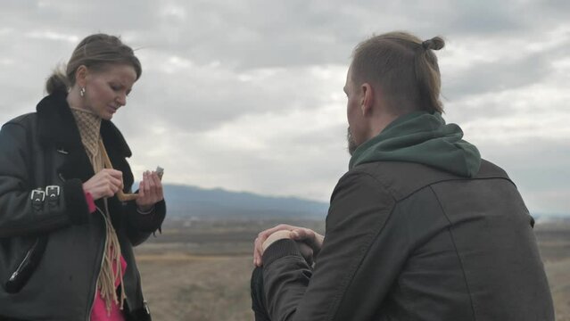 attractive young woman and man with braided hair practicing Rape ceremony in the mountains at sunset. Preparation for the ceremony, filling the snuff tube with herbal powder from the palm