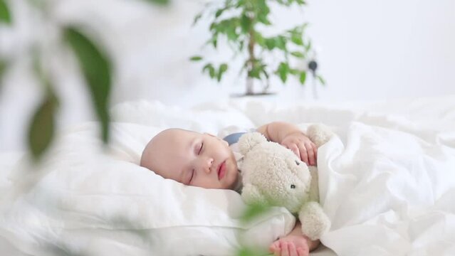 Portrait of a little child lying on a white bed with a teddy bear in his hands on a background of green grass with space for text for advertising tenderness