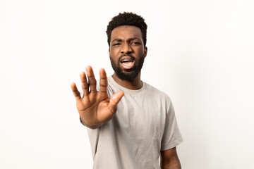 Portrait of an African American man showing a stop hand sign, displaying rejection or warning on a white backdrop.