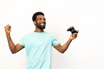 An exuberant African American man celebrates a victory, fist pumped and holding a gaming controller, isolated on a white background, expressing positive emotions. - 745842662