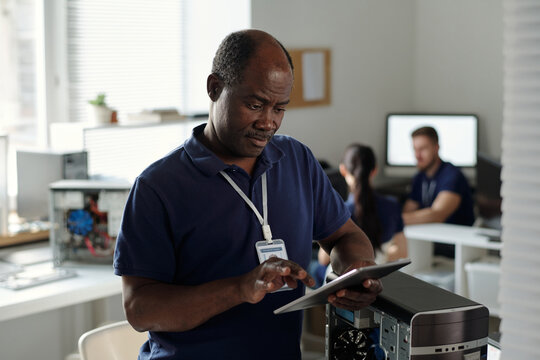 Mature engineer or technician of repair center using tablet while standing by disassembled computer processor and reading online manual