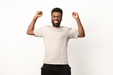 An ecstatic African American man raises his arms in victory, exuding happiness and success on a white backdrop. - 745843089
