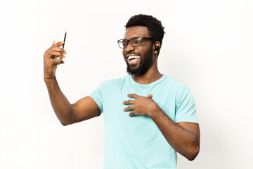 Happy African American man in casual attire using a smartphone and earbuds, isolated on a white background. Technology in everyday life and joyful expression captured in a studio setting. - 745843643