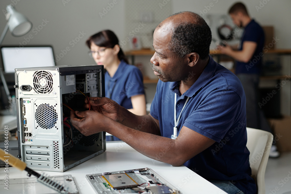 Poster Professional mature technician sitting by workplace in repair service office and identifying technical problems of disassembled computer processor