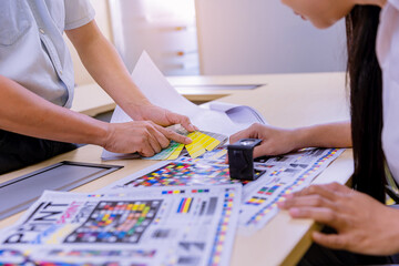 Crop image of worker checking print quality of media graphics proof print and color tone in...
