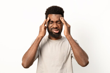 Young man with eyes closed, touching his temples in discomfort, suggesting headache, stress or migraine against a plain white background. - 745845295