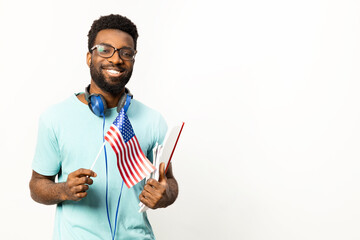 Joyful African American man with headphones around neck holding an American flag, portraying a relaxed, patriotic and happy lifestyle against a white background. - 745845660