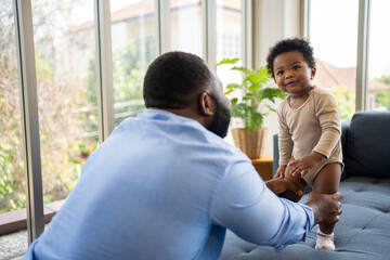 Portrait Of Happy African American Dad With Cute Little Baby Girl on couch at home in the living room, caring father smiling and amusing his girl while sitting on the couch, happy family