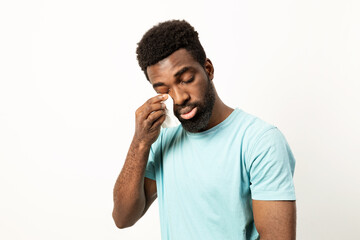 Emotional African American man using a tissue to wipe away tears, with a somber expression on a...