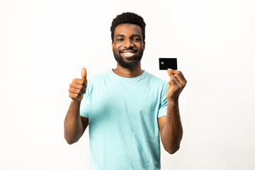 Online shopping. Afro American man showing credit card and making thumbs up gesture, isolated on white background. Represents online shopping, payment approval and consumer satisfaction. - 745849699