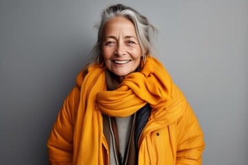 Happy senior woman in warm yellow jacket, isolated on grey background.