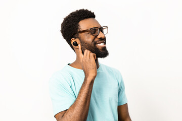 African American man enjoying music with wireless earbuds. Smiling male in casual clothing with glasses, isolated on a white background, experiencing joy. - 745850881