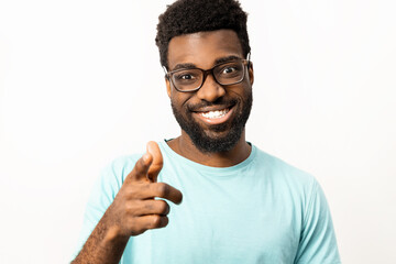 African American man wearing glasses and a casual t-shirt smiling and pointing towards the camera on an isolated white background, representing positivity and friendliness. - 745851064