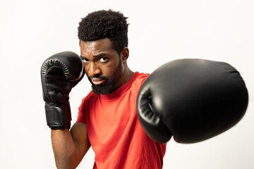A focused African American man in a red shirt, wearing boxing gloves, adopts a fighting stance...