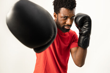 An African American male engaging in a fitness routine, showcasing intensity and determination with boxing gloves, isolated on a white background. - 745851615