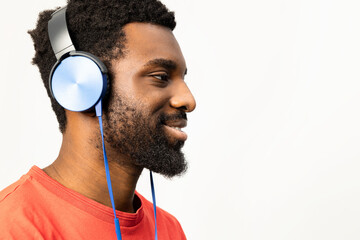 Side profile of a joyful African American man wearing blue headphones and a red shirt, isolated on...