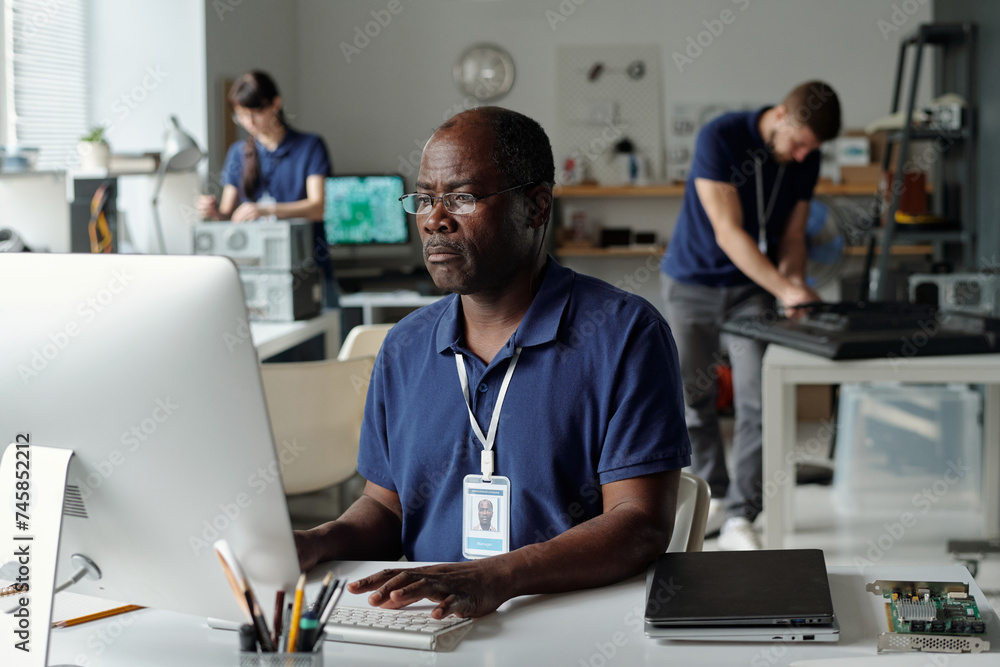 Poster serious mature male worker of repair service center touching keys of desktop computer keyboard and l