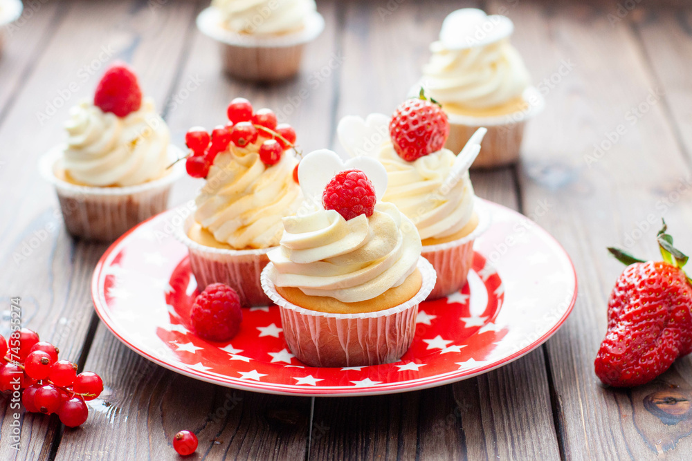 Wall mural vanilla cupcakes decorated with fresh strawberry, raspberry and red currant on rustic wooden backgro