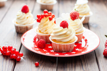 Vanilla cupcakes decorated with fresh strawberry, raspberry and red currant on rustic wooden background