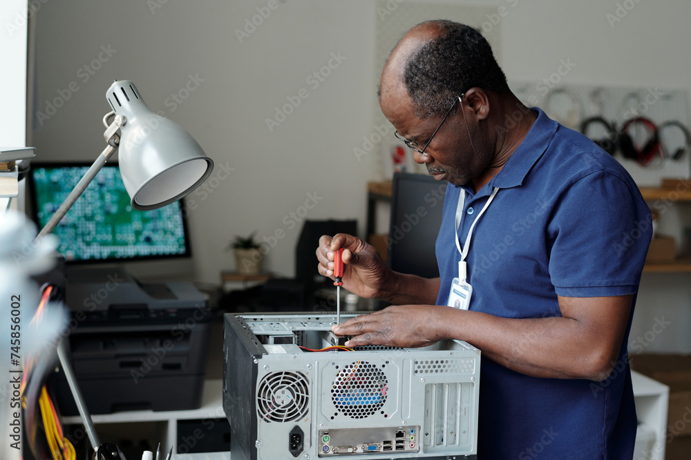 Poster side view of mature professional technician with screwdriver in hand fixing details of computer hard