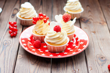 Vanilla cupcakes decorated with fresh strawberry, raspberry and red currant on rustic wooden background