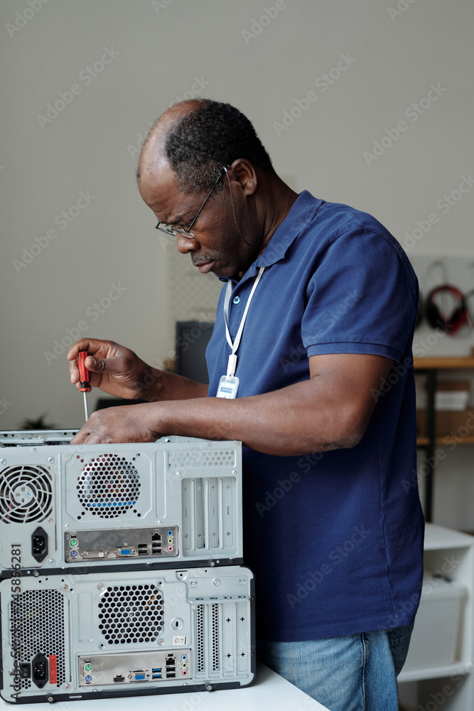 Poster professional male technician fixing details of computer hardware with screwdriver while standing by 