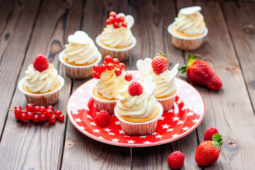 Vanilla cupcakes decorated with fresh strawberry, raspberry and red currant on rustic wooden background