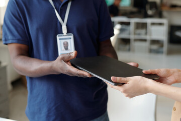Hands of unrecognizable mature African American repairman passing laptop to young female client after repairing device